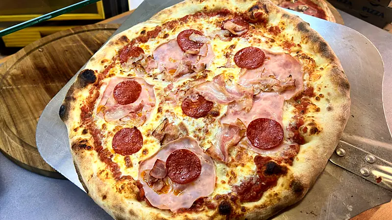 Upečená pizza se šunkou a salámem na lopatě u vitríny